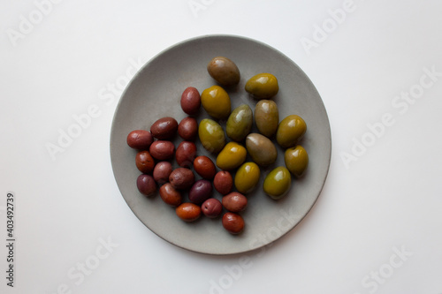 Green and purple olives on grey concrete plate isolated on white background from a high angle view