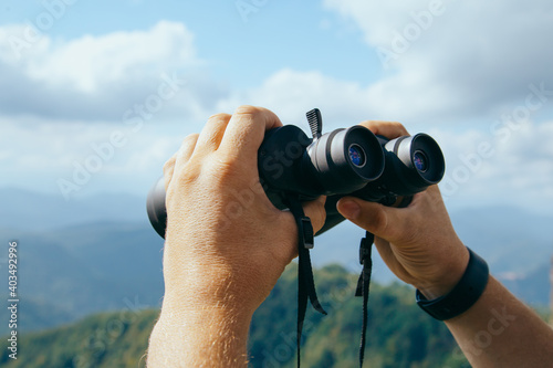 Hands holding binoculars on mountains forest nature background, looking through binoculars, travel, search and search concept. © Nana_studio