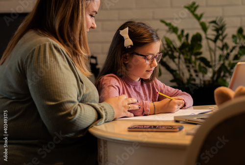 Mother helps her daughter with homework sitting at the living room table at home.