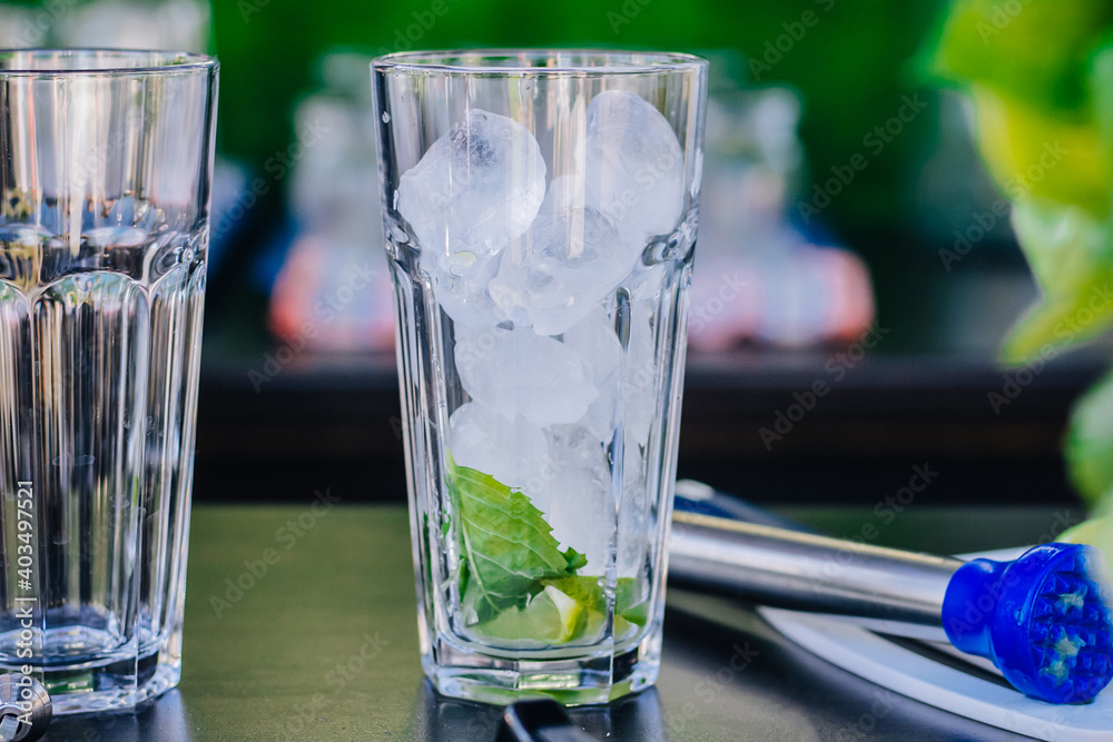 Close-up of a glass beaker with ice cubes and lime wedges stands on the table. Outdoor party. Close-up of a glass beaker with ice cubes and lime wedges stands on the table. Outdoor party.