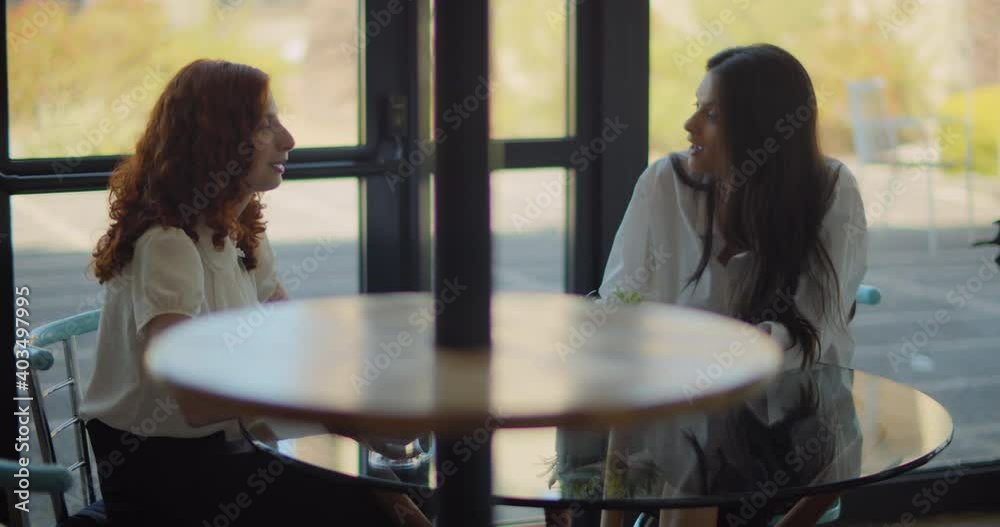 Two women coworkers talking to each other while meeting in the small cafe. Slow motion. Two women coworkers talking to each other while meeting in the small cafe. Slow motion.