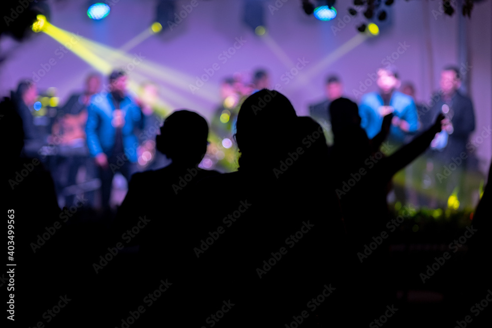 Beautiful shot of the silhouette of peoples dancing in the club with a band performing on the stage