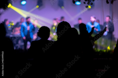Beautiful shot of the silhouette of peoples dancing in the club with a band performing on the stage © Wirestock Exclusives