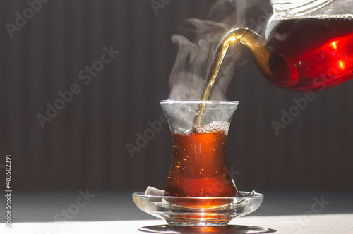 Glass cup of brewed black turkish tea pouring from teapot, traditional hot drink concept photo