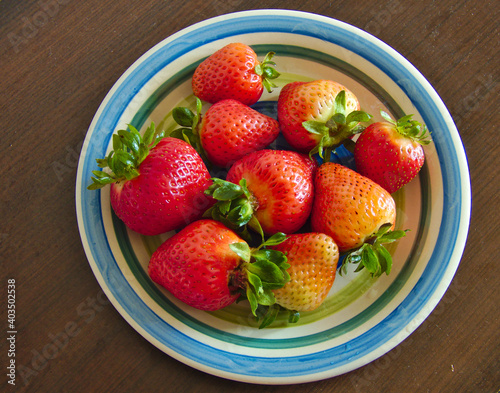 round yellow white and blue plate with red orange and yellow strawberries on a brown table