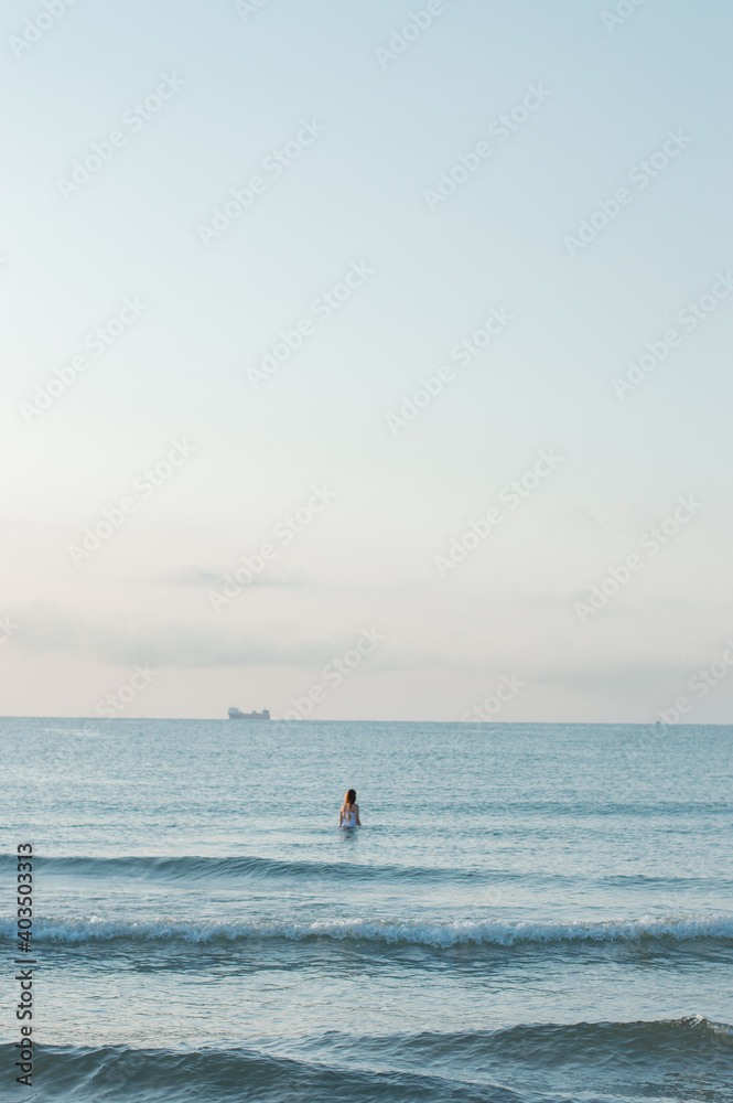 Vertical shot of a female standing in the middle of the ocean