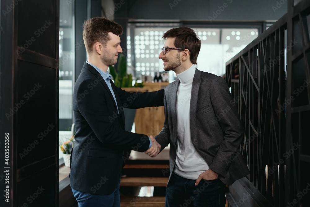 Smiling young business partners in business casual wear looking at each other while shaking hands after agreement. Greeting concept Smiling young business partners in business casual wear looking at each other while shaking hands after agreement. Greeting concept