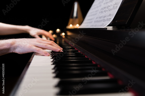 Fotografia Hands playing the piano keyboard closeup and candle light bokeh background