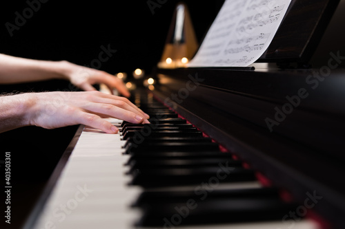 Hands playing the piano keyboard closeup and candle light bokeh background. Male pianist learning to play the piano instrument and beautiful music. Reading sheet music with metronome