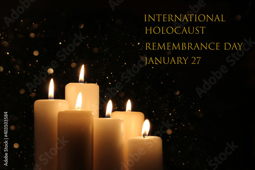International Holocaust Remembrance Day January 27. Burning six white candles with lights glow on black background.