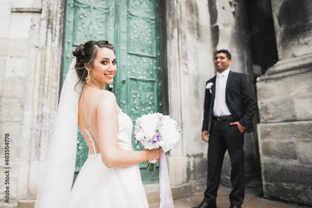 Lovely happy wedding couple, bride with long white dress posing in beautiful city Lovely happy wedding couple, bride with long white dress posing in beautiful city