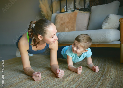 mom and son play sports at home. they perform the plank exercise. a smile on their faces.
