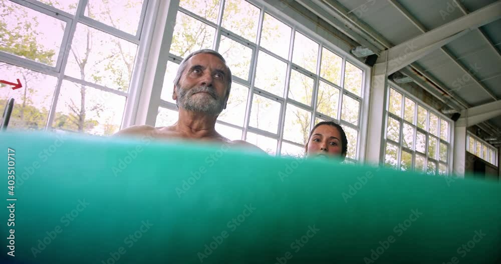Instructor helping senior man raising pool noodle in aerobics class