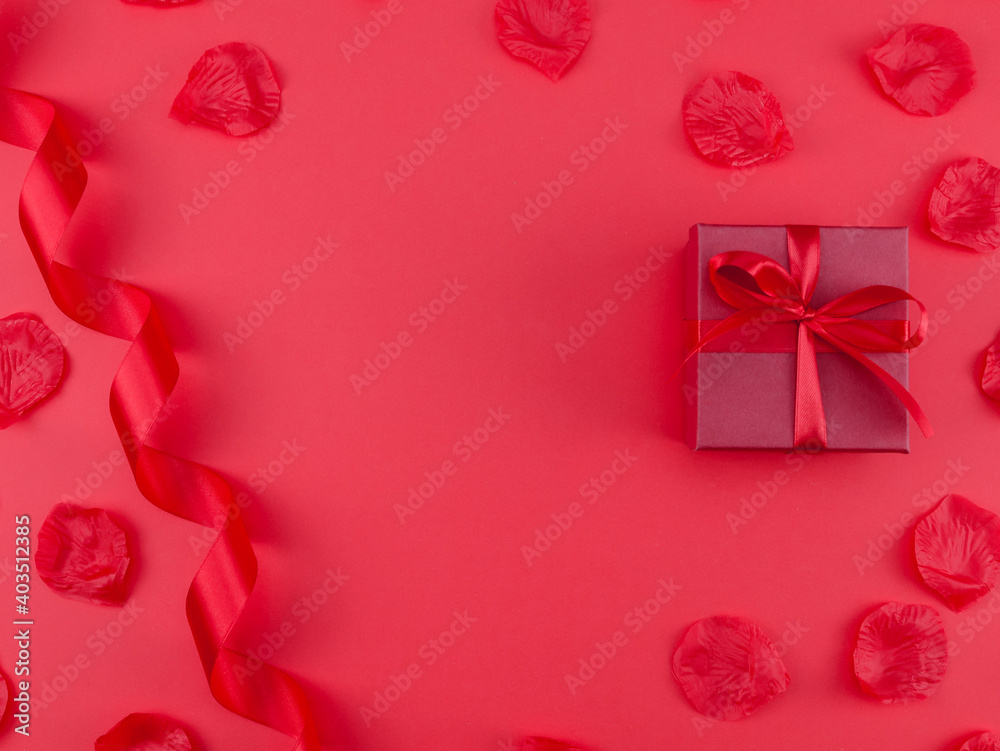 
Gift and rose petals.
Gift, ribbon and rose petals on a red background with place for text in the middle, top view close-up.