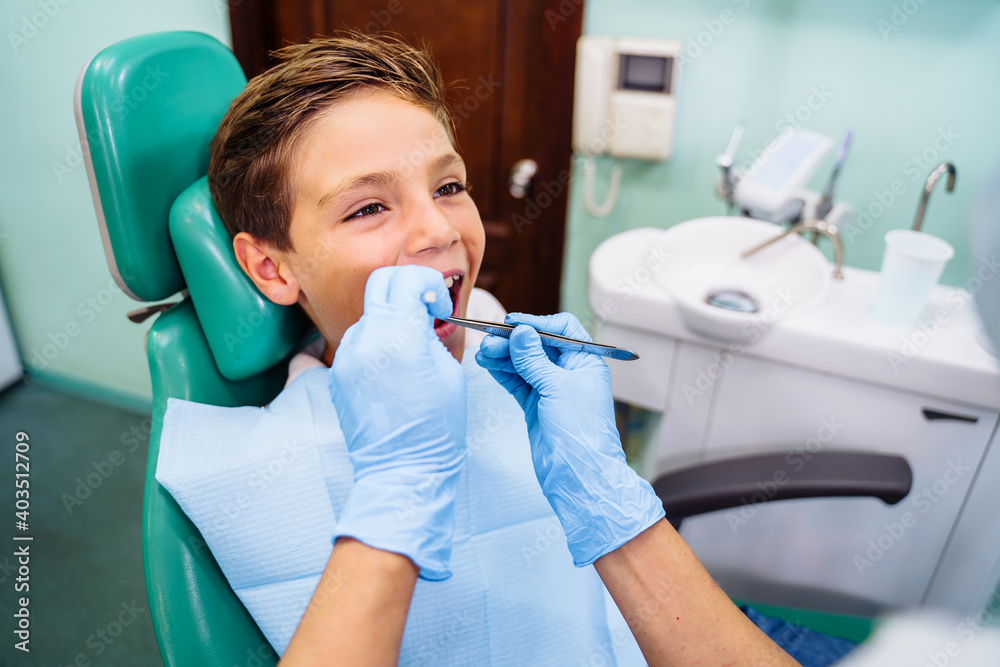 A small patient with an open mouth at a dentist appointment in a modern clinic. Hands of unrecognizable pediatric dentist doing examination procedure for smiling cute boy in hospital A small patient with an open mouth at a dentist appointment in a modern clinic. Hands of unrecognizable pediatric dentist doing examination procedure for smiling cute boy in hospital