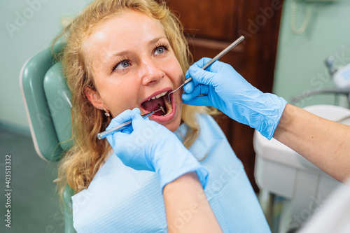 Cute european girl at the dentist s appointment. Close-up of a dentist s hands with medical instruments. Drill and tweezers in action. Selective focus. Dental care  taking care of teeth