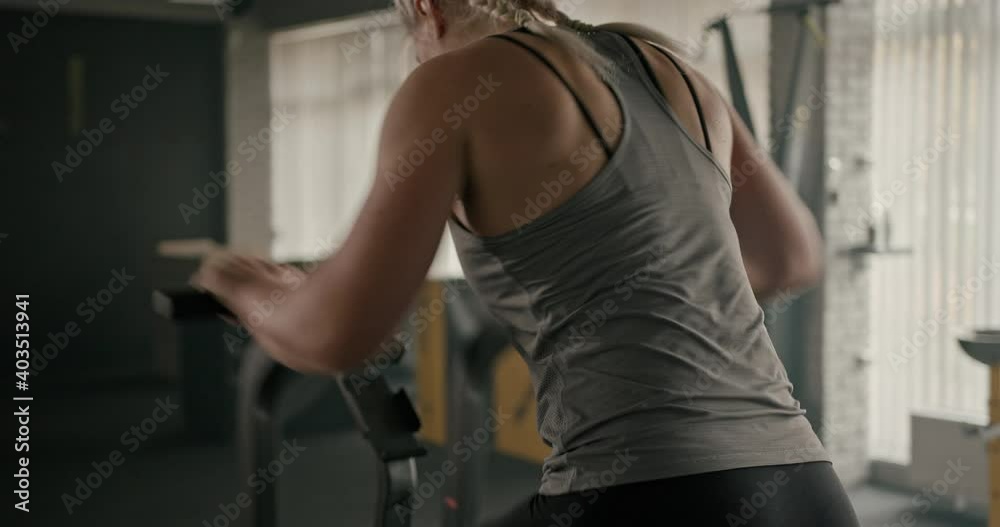 Muscular sportswoman breathing heavily and exercising on stepping machine during intense fitness training in gym Muscular sportswoman breathing heavily and exercising on stepping machine during intense fitness training in gym