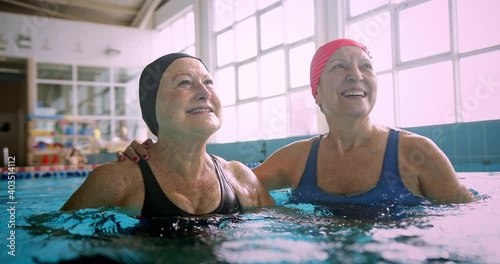 Two senior women embracing together in swimming indoor pool