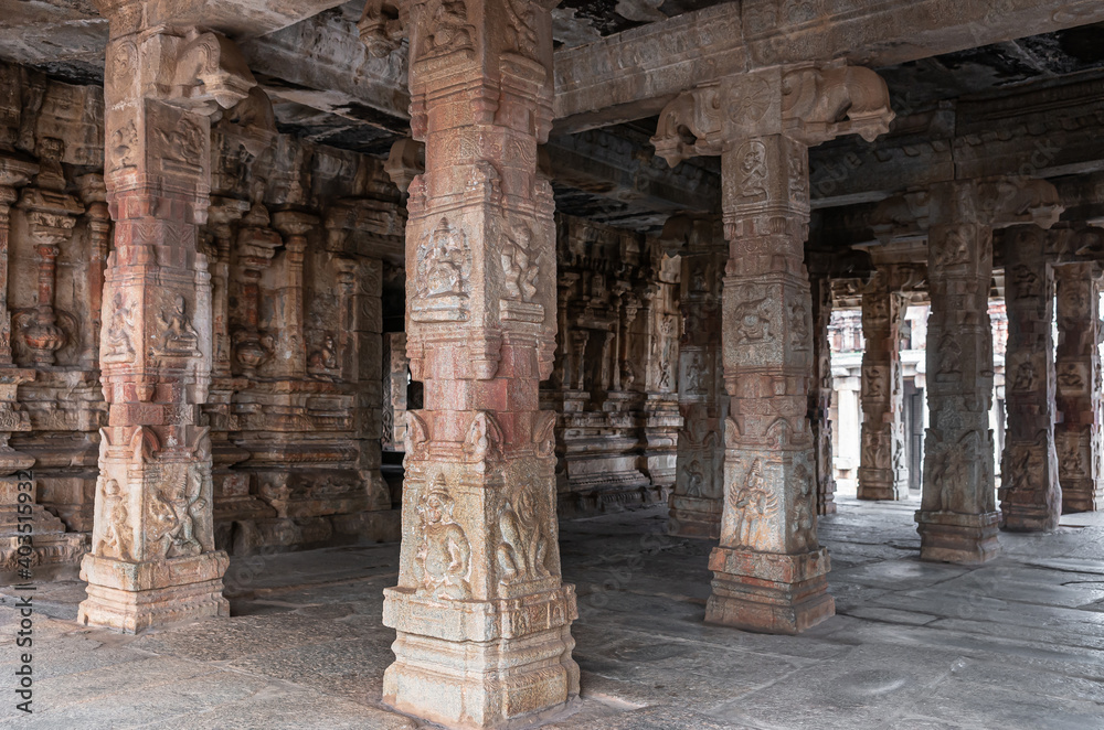 Hampi, Karnataka, India - November 5, 2013: Sri Krishna temple in ruins. Brown reddish sculpted pillars supporting mandapam in front of sanctum.