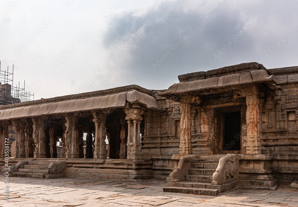 Hampi, Karnataka, India - November 5, 2013: Sri Krishna temple in ruins. Brown stone baluster steps lead into Mandapam and inner sanctum under gray cloudscape. Scaffold on main entrance gopuram.
