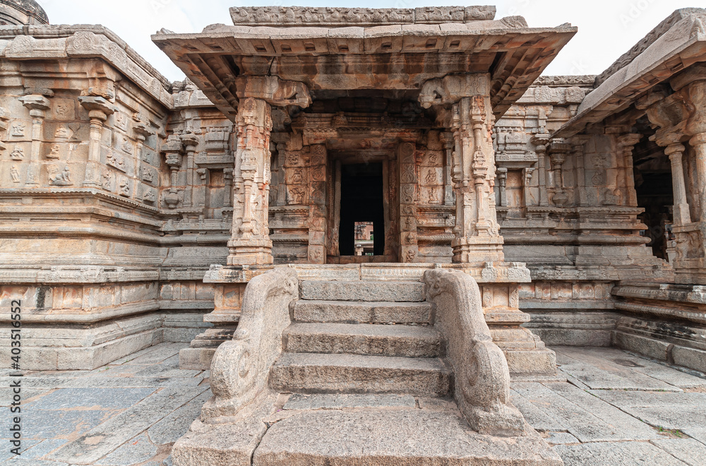 Hampi, Karnataka, India - November 5, 2013: Sri Krishna temple in ruins. Brown stone steps with balusters lead to entrance to inner sanctum under silver sky. Look through to other side.