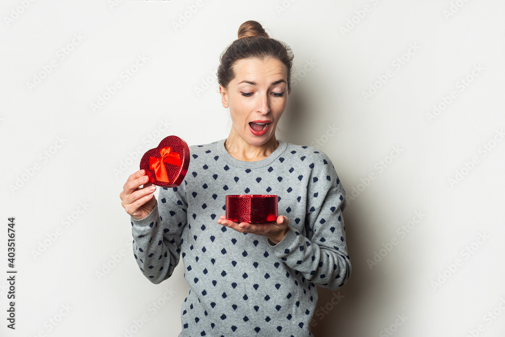 Surprised young woman rejoices with a gift on a light background. Valentine's day, birthday. Banner Surprised young woman rejoices with a gift on a light background. Valentine's day, birthday. Banner