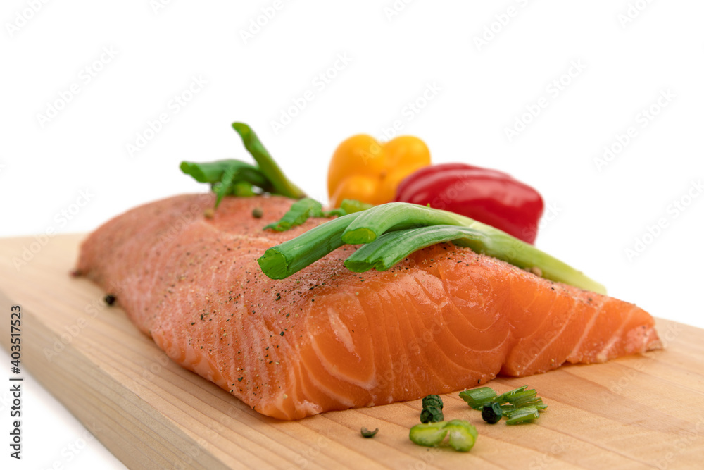 close up of a piece of salmon with green onions, peppers and pepper corns on a cedar plank close up of a piece of salmon with green onions, peppers and pepper corns on a cedar plank