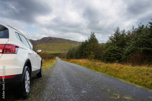 Big white family car parked off small road by a forest and a mountains, Sligo, Ireland. Concept travel and explore nature.
