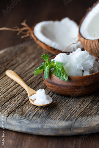 Coconut oil in a small wooden bowl and small wooden spoon with a cracked coconut in behind.