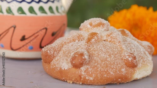 Closeup of pan de muerto covered with sugar, Mexican sweet bread near coffee cup and cempasuchil flower on table enjoyed traditionally during Day of the Dead holidays in Mexico