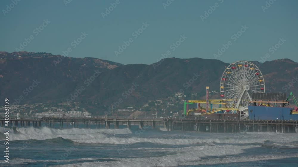 Powerful waves crash into shore and the pier with the famous Santa Monica Ferris Wheel and landscape in the distance - slow motion Powerful waves crash into shore and the pier with the famous Santa Monica Ferris Wheel and landscape in the distance - slow motion