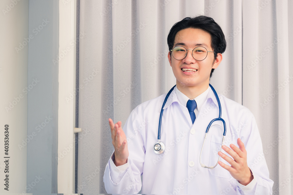 Portrait of Happy Asian young doctor handsome man smiling in uniform with stethoscope talking online video conference call or facetime raise his hand to explain, healthcare medicine concept Portrait of Happy Asian young doctor handsome man smiling in uniform with stethoscope talking online video conference call or facetime raise his hand to explain, healthcare medicine concept