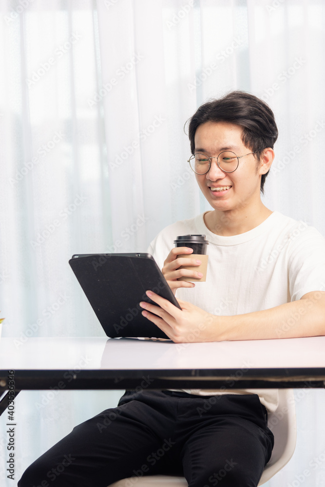 Happy Asian young business handsome man work from home office wear glasses, t-shirt comfortable he smiling and using a black modern smart digital tablet computer to read email or learning on desk Happy Asian young business handsome man work from home office wear glasses, t-shirt comfortable he smiling and using a black modern smart digital tablet computer to read email or learning on desk