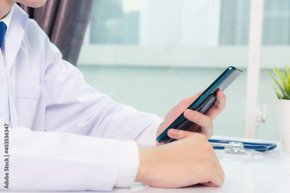 Asian doctor young handsome man smiling using working or holding with digital smart mobile phone at hospital desk office, Technology healthcare medical concept