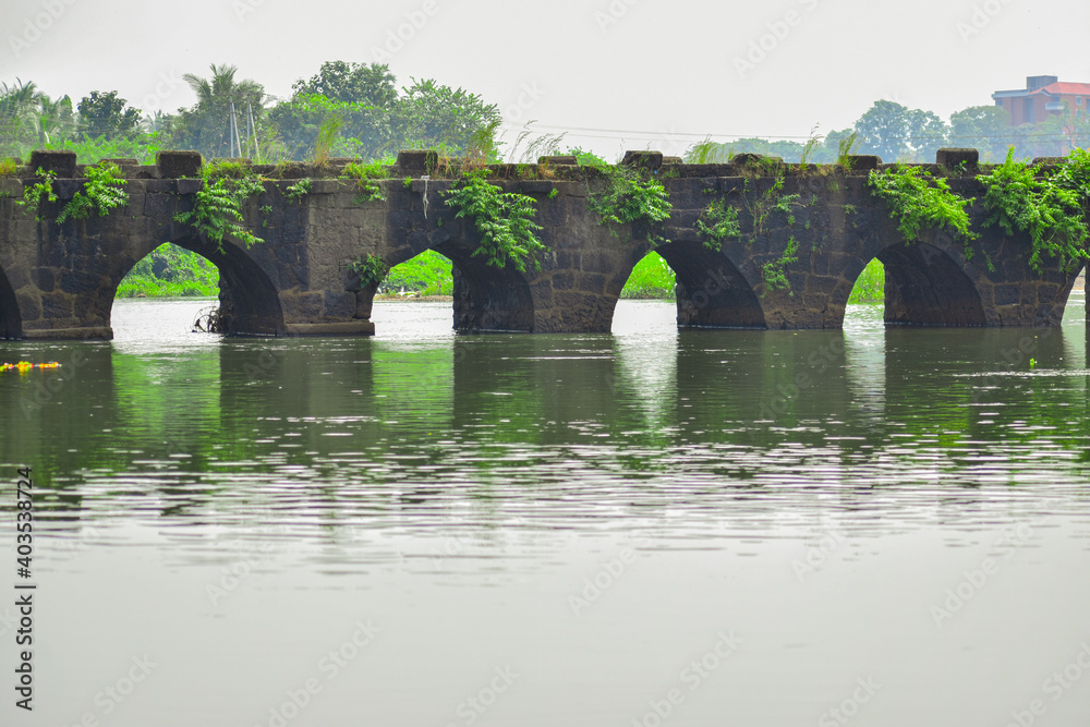 stone arch bridge over river and reflection of bridge in water with greenery around it in panvel city,Maharashtra,India