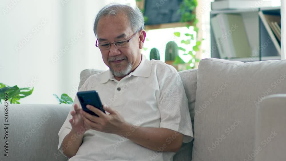 Happiness elderly asian man sitting on sofa using mobile phone and social media smile at home,Senior lifestyle at home concept