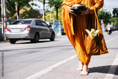 Buddhist monk holding alms bowl walking on the road in the morning.
