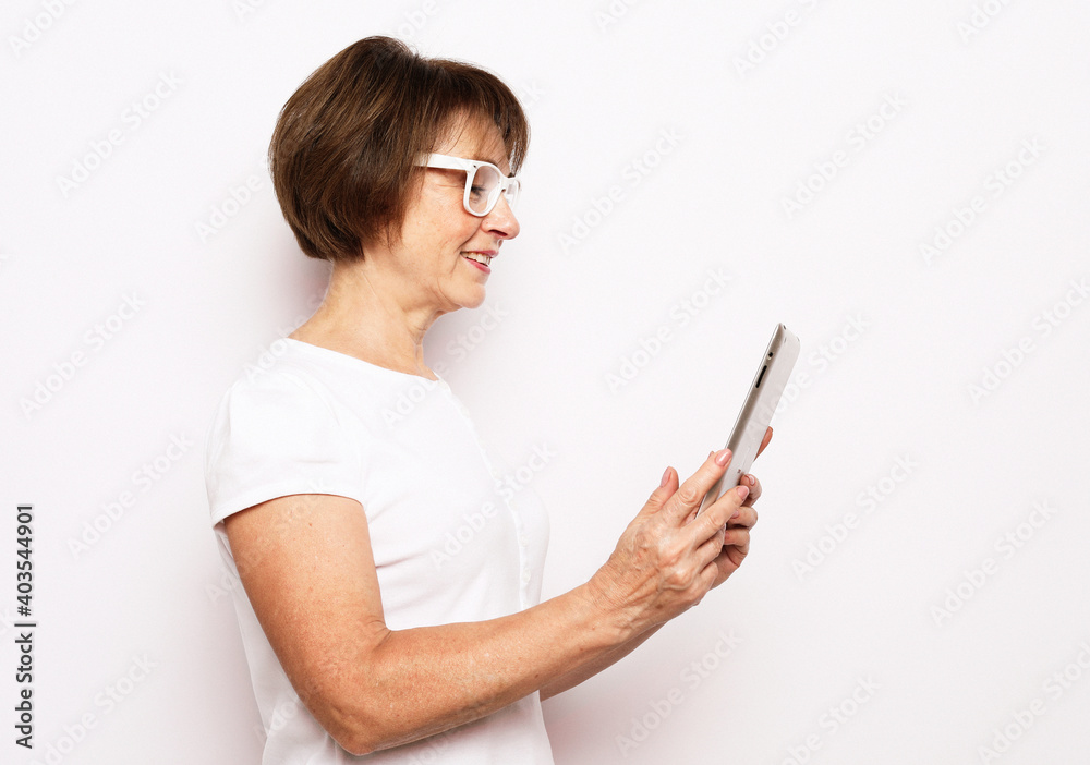 Old smiling business woman wearing glasses, reading browsing using holding tablet. Isolated over white background. Old smiling business woman wearing glasses, reading browsing using holding tablet. Isolated over white background.