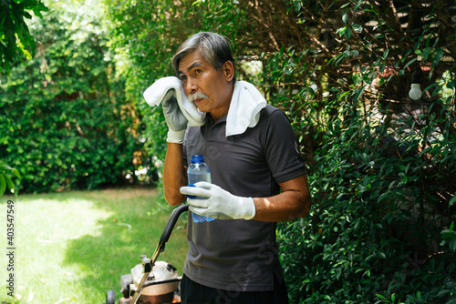 Senior elderly man take a break drinking water from bottle after mowing the lawn at park.
