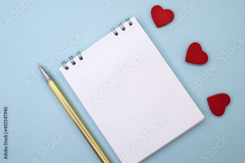 A notebook with a white sheet lies on a blue background about three hearts and a pen . Greeting card. Space for text