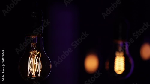 Vintage decorative light bulbs hang in the dark and pulsate with light and go out against a blurred background with bokeh.