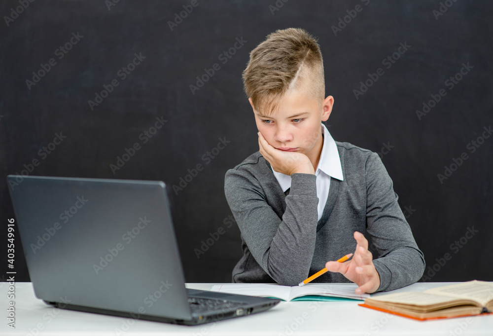 Pensive teen boy uses laptop at school. Distance education concept Pensive teen boy uses laptop at school. Distance education concept
