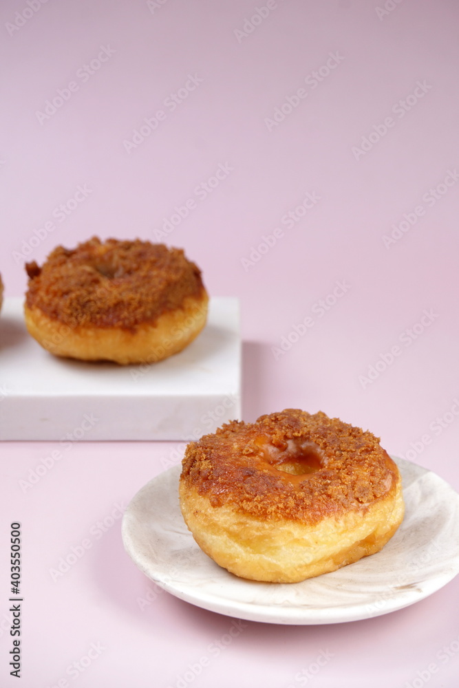 Grainy Donat or Donut or Doughnut with caramel and Lotus biscuit crumbs. Selective focus, pink pastel background