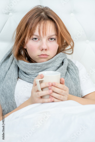 Sad sick girl sitting on the bed holding a mug of hot tea