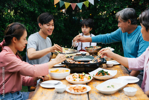 Cheerful asian family enjoy eating thai BBQ and local food together at yard.