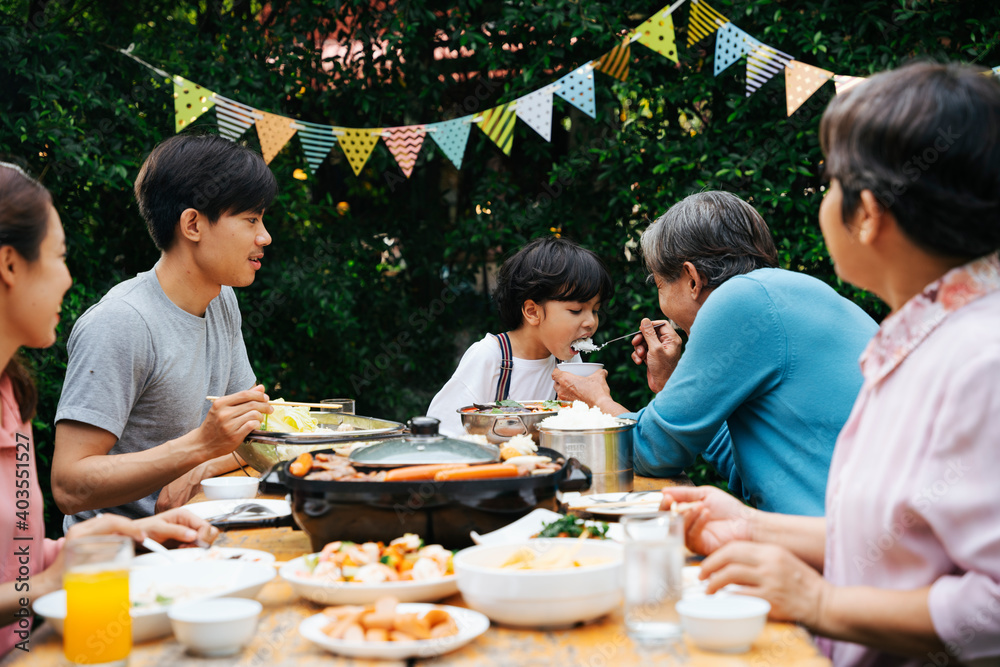 Asian family eating BBQ dining outdoor at yard to celebrate party.