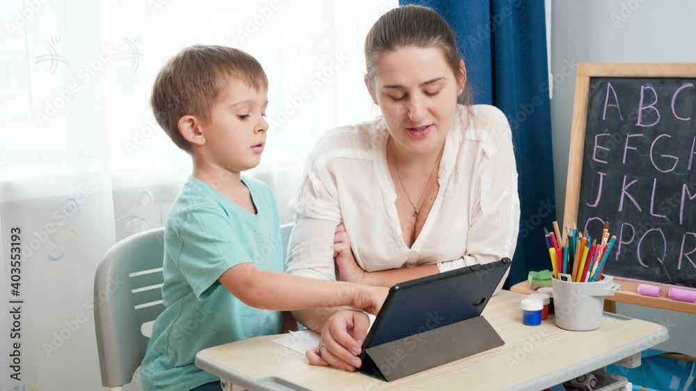 Young female teacher with little boy using tablet computer while learning alphabet at school classroom. Parenting and remote school education at home. Young female teacher with little boy using tablet computer while learning alphabet at school classroom. Parenting and remote school education at home.