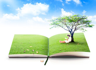 Open book with green grass and woman sitting reading under tree on pages for education and environment concept in blue sky background with clouds isolated on white background