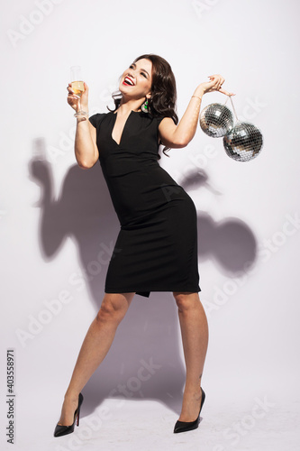 Young fashionable brunette woman wearing bright dress holding disco balls and a glass of champagne. © Raisa Kanareva