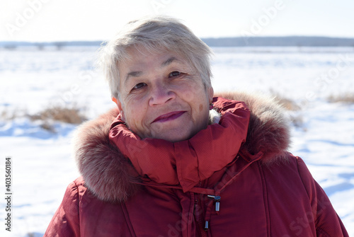 Portrait of Russian senior woman sincerely smiling and looking at the camera against snowy field. winter